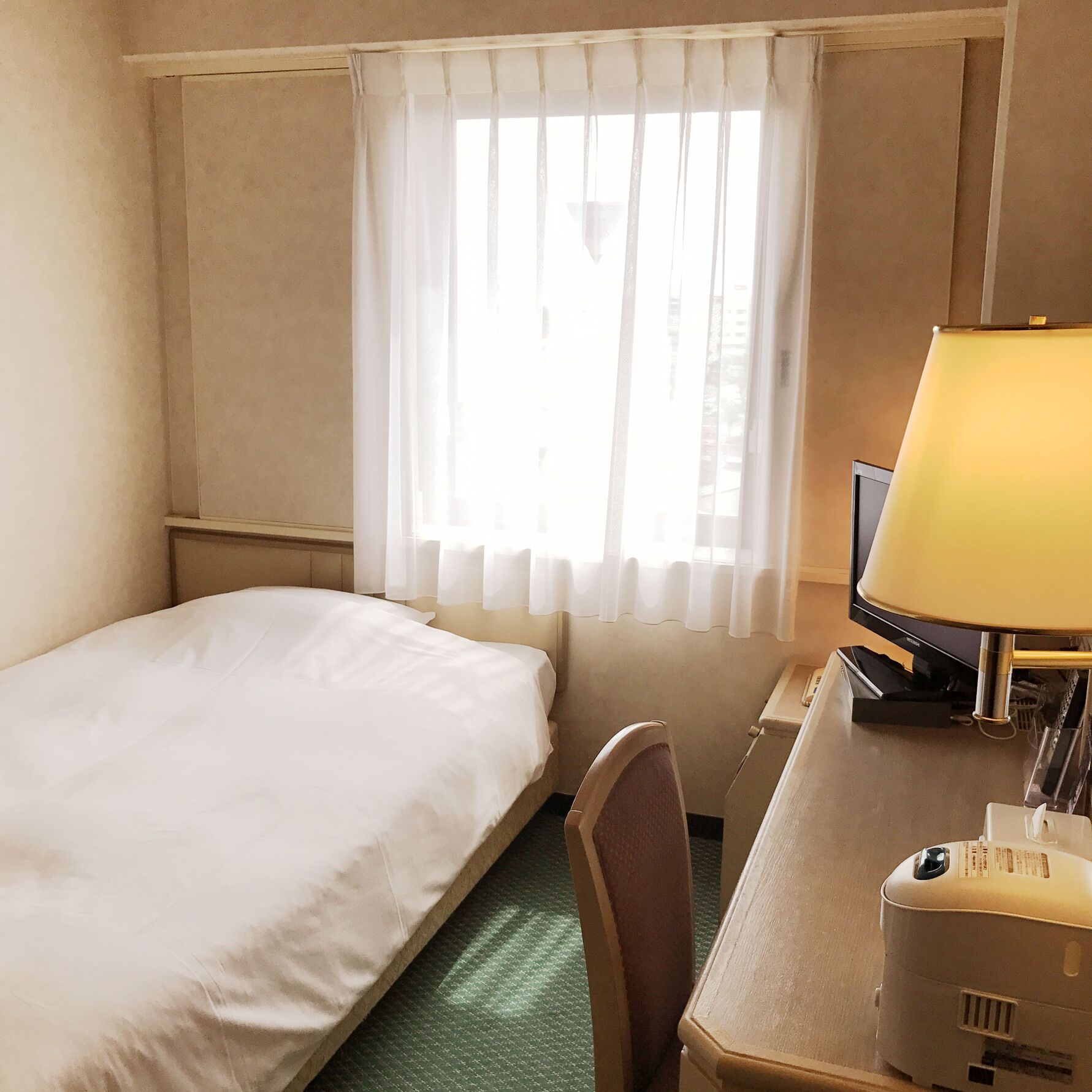 Ein Hotelzimmer mit einem Bett, einem Schreibtisch mit Lampe, einem Fernseher und einem Sessel.