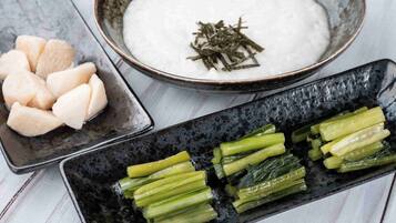 A bowl of white rice with seaweed garnish, a plate of sliced green vegetables, and a bowl of sliced white radish.