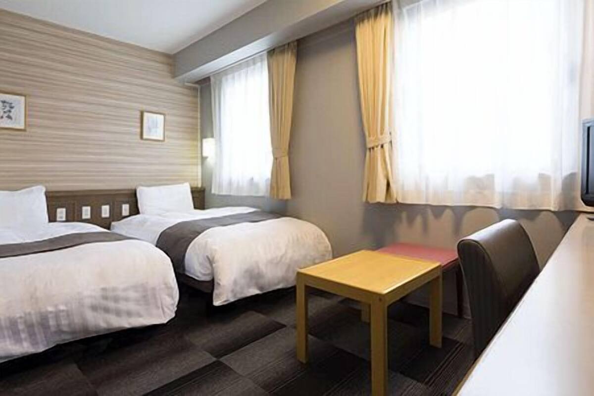 Hotellihuone, jossa on kaksi sänkyä, pieni puinen pöytä ja sohva.