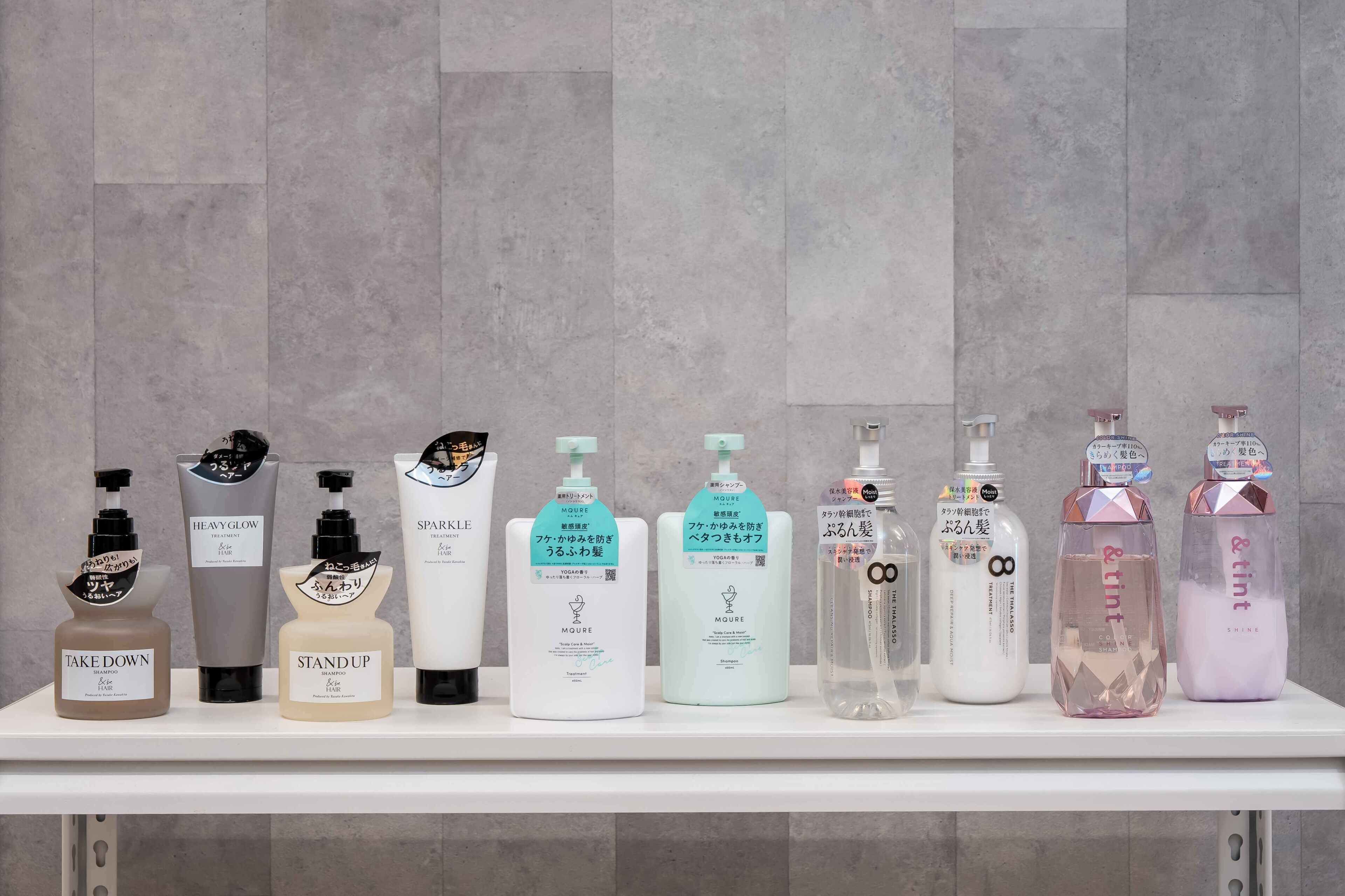 A row of toiletry bottles on a white shelf against a grey tiled wall.