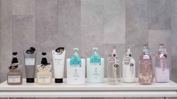 A row of toiletry bottles on a white shelf against a grey tiled wall.