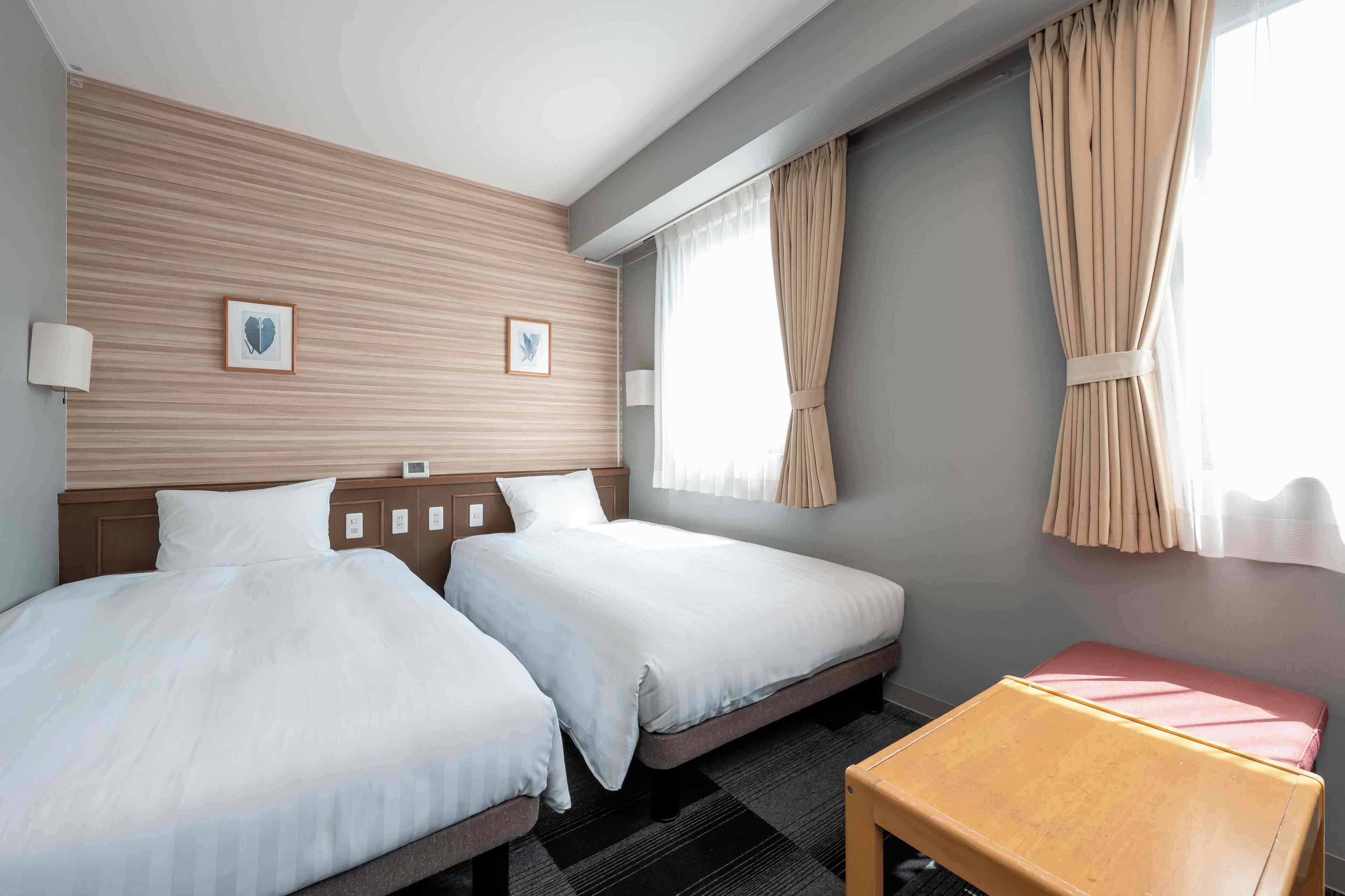 Habitación de hotel con dos camas, una mesita y una ventana con cortinas.
