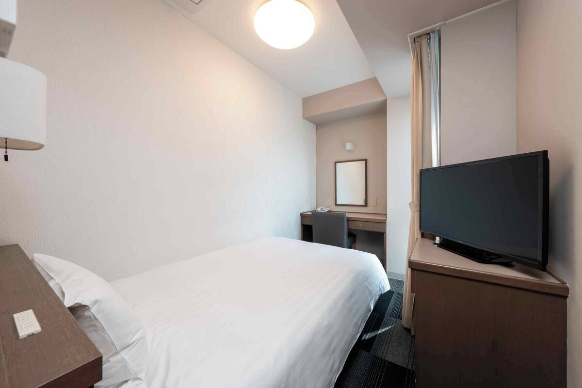 Hotellihuone, jossa on sänky, työpöytä, televisio ja peili.