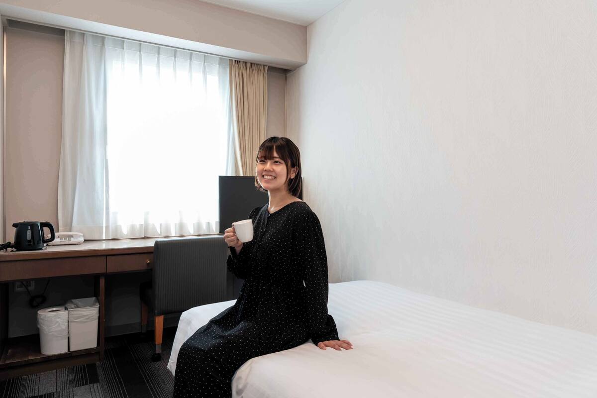 Hotellihuone, jossa on sänky, työpöytä, jossa on puhelin ja kahvinkeitin, sekä ikkuna, jossa on verhot.