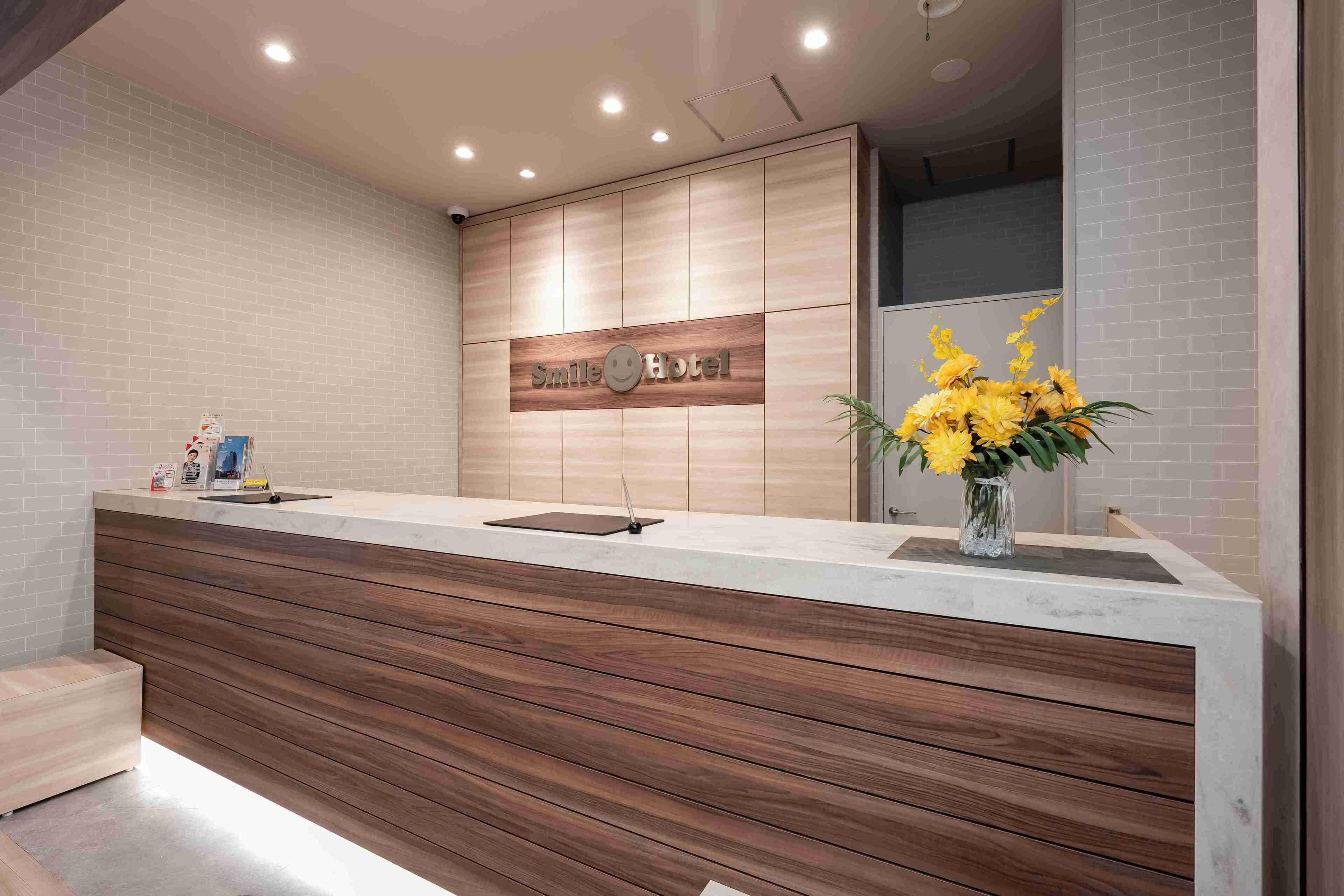 A reception area with a wooden counter, a wall-mounted smiley face, and a vase of yellow flowers.
