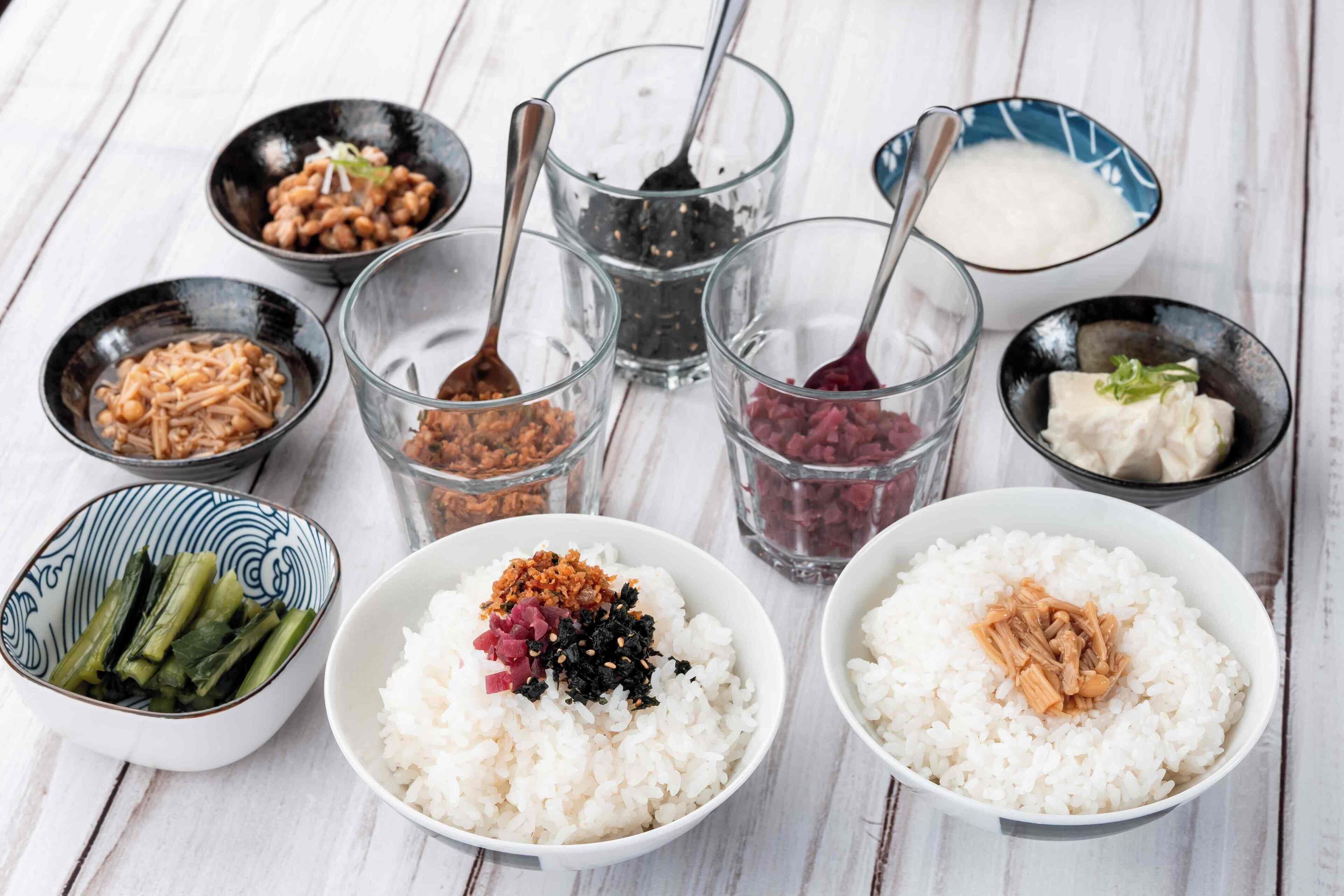 A table with bowls of rice topped with various ingredients, and small bowls containing different condiments.