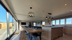 A modern kitchen with a wooden dining table, bar seating, and large windows. - Eastgate Barn, Ashlin Farm Barns (Lincoln)