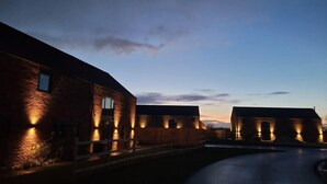 A brick building with multiple arched windows and a well-lit exterior at dusk. - Eastgate Barn, Ashlin Farm Barns (Lincoln)