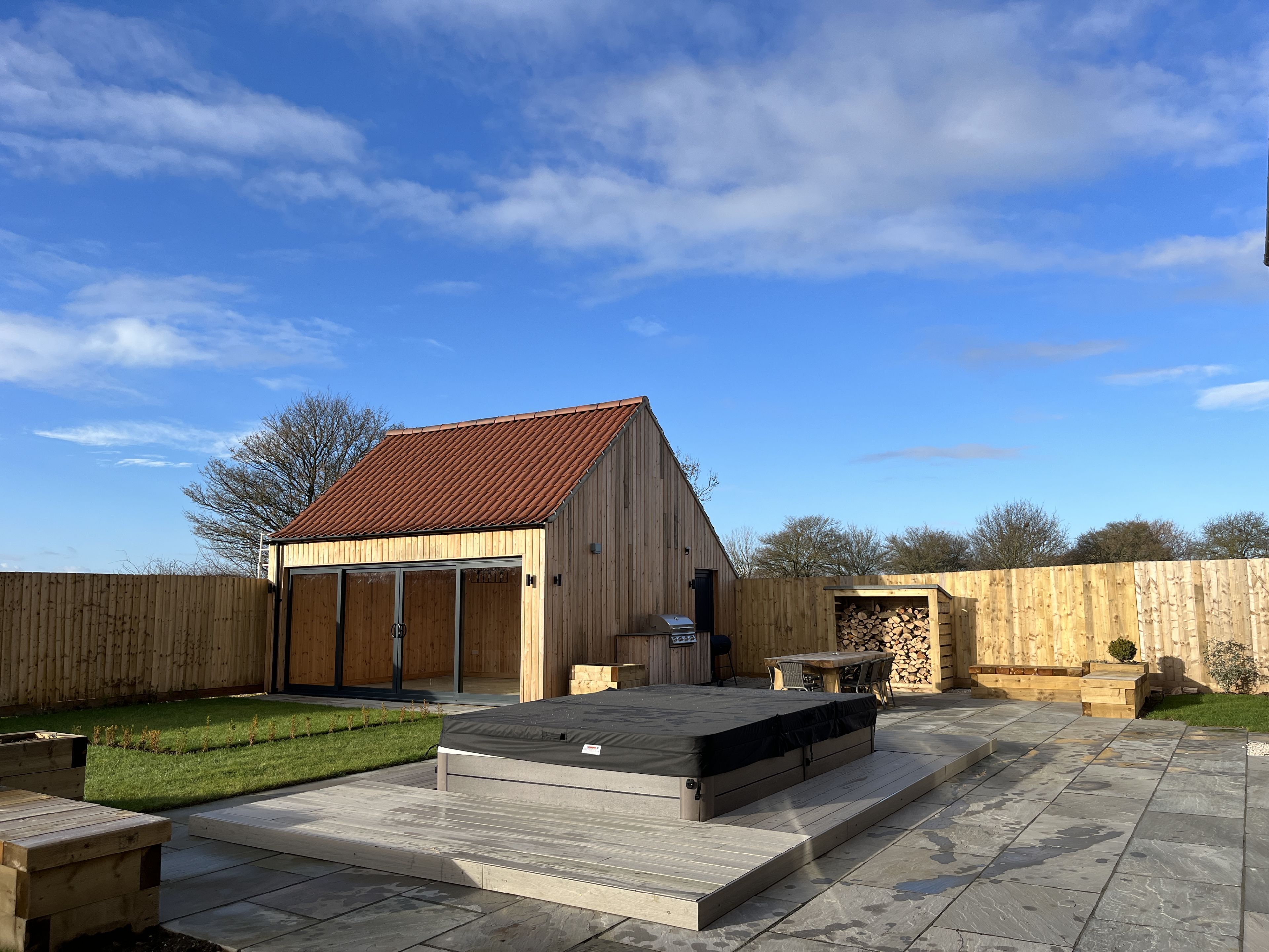 Ein Garten mit einer Holzterrasse, einem Grill und einer überdachten Veranda.