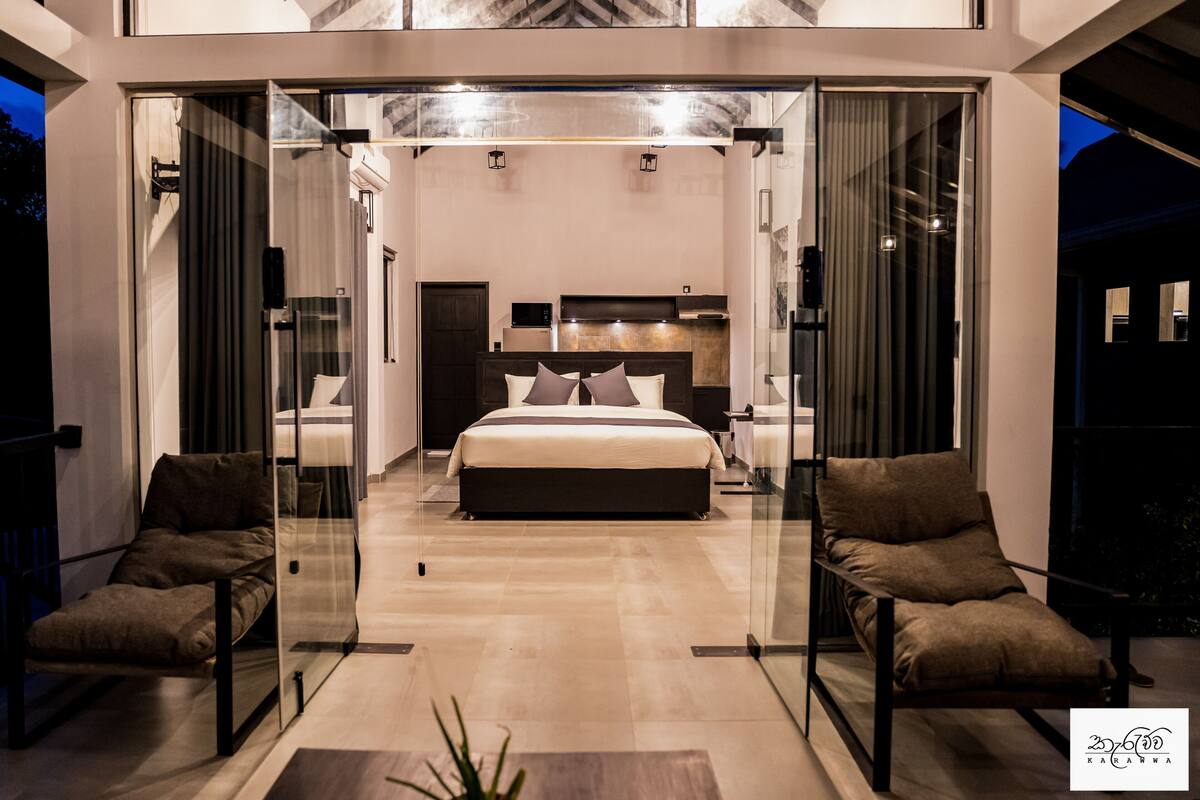 A modern bedroom with a large bed, glass doors, and a seating area.