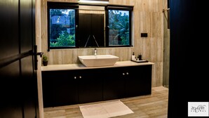 A modern bathroom with a large window, a vessel sink, dark cabinetry, and a wooden floor. - Karawwa Luxury Villas  (Hikkaduwa)