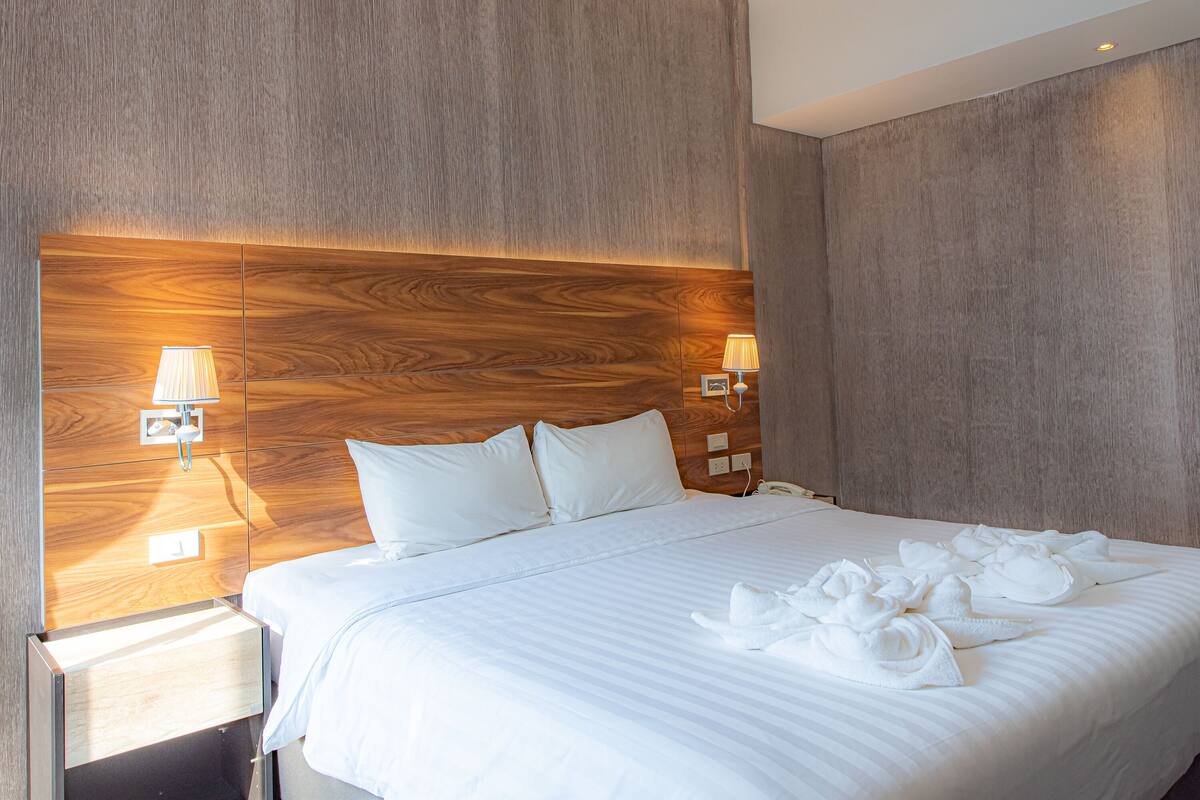 A hotel room with a large bed, wooden headboard, bedside lamps, and neatly arranged towels.