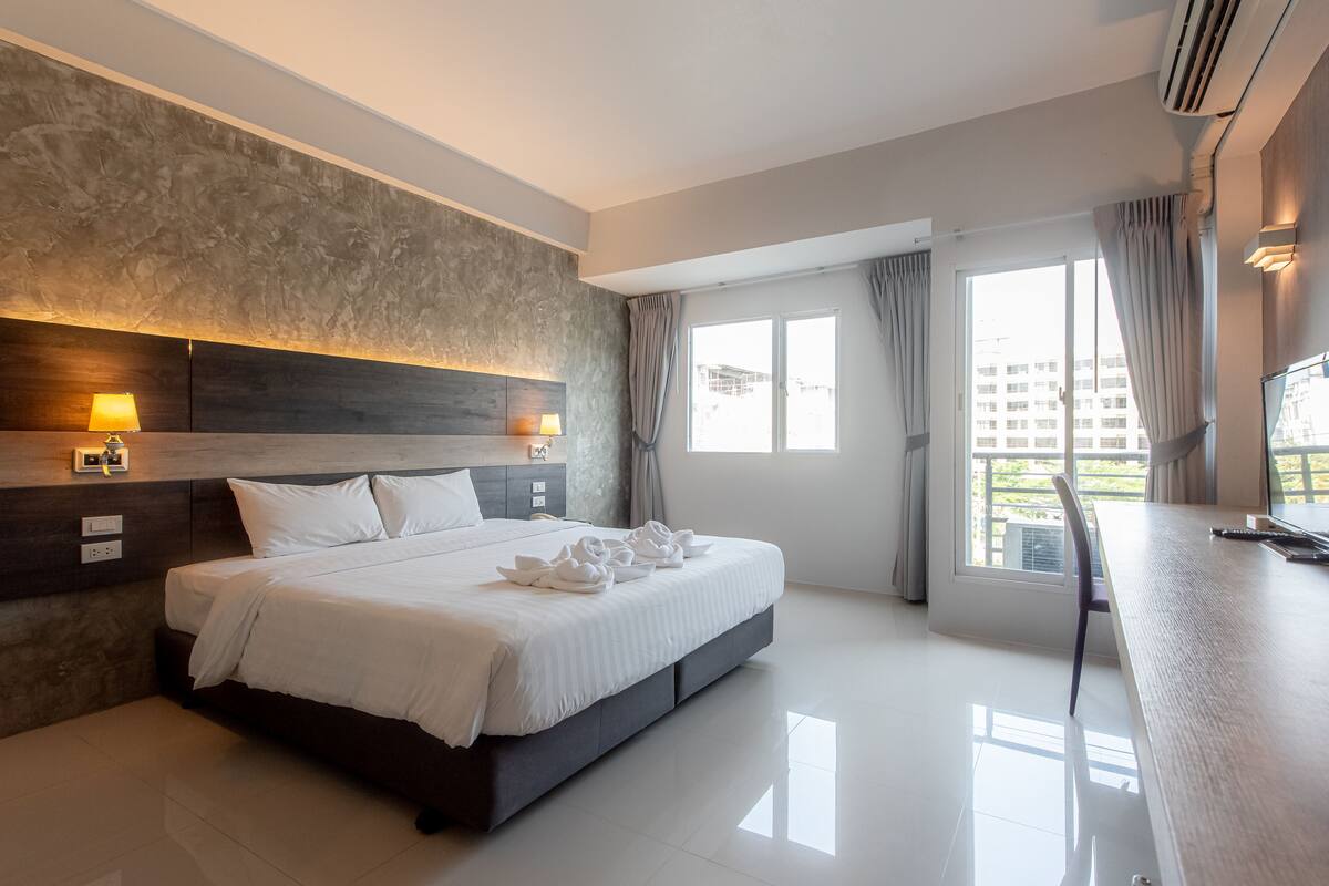 A modern hotel room with a large bed, bedside lamps, a desk, and a view of the city.