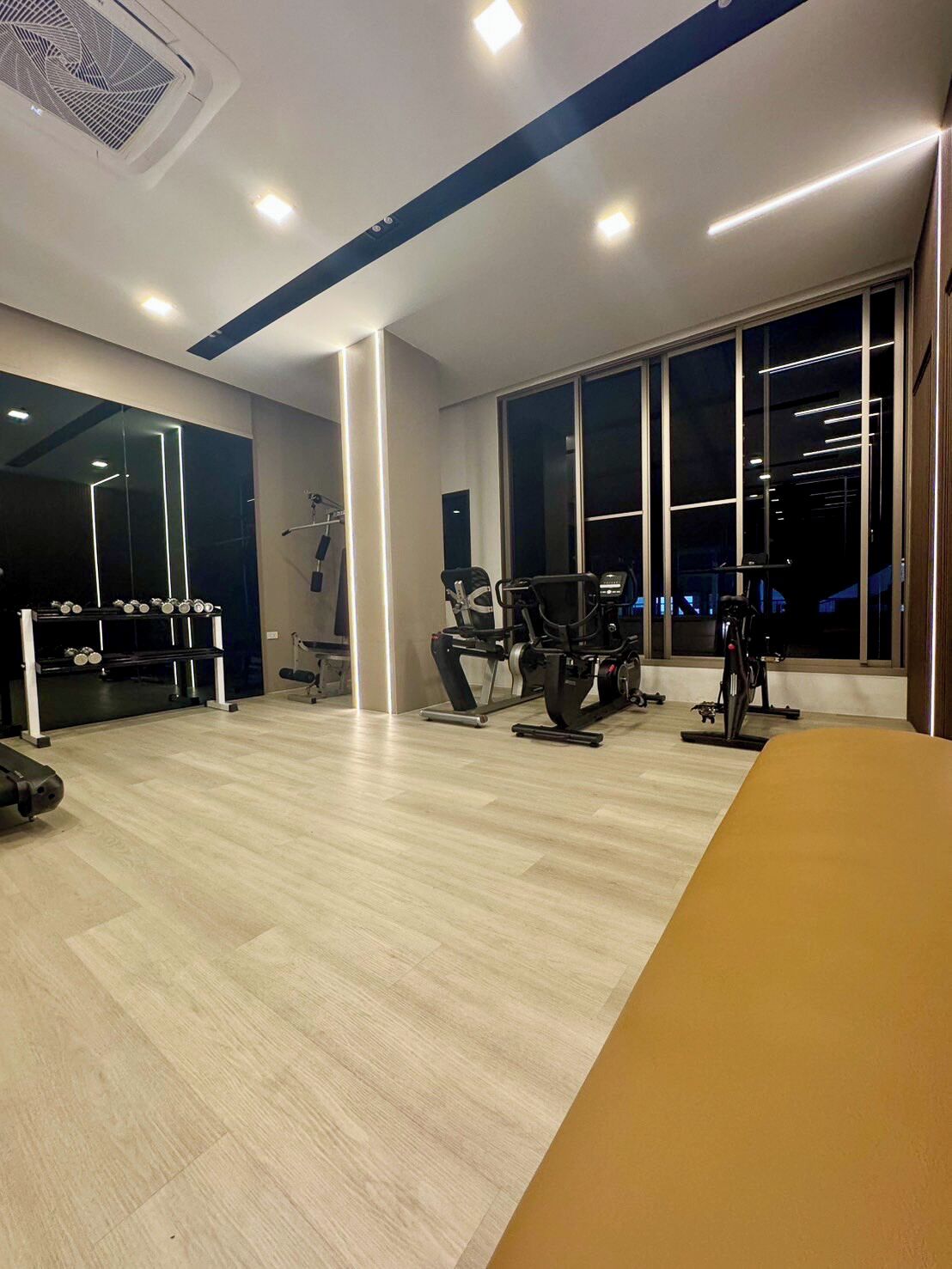 Un gimnasio moderno con equipo de ejercicio, ventanas amplias y suelo de madera.