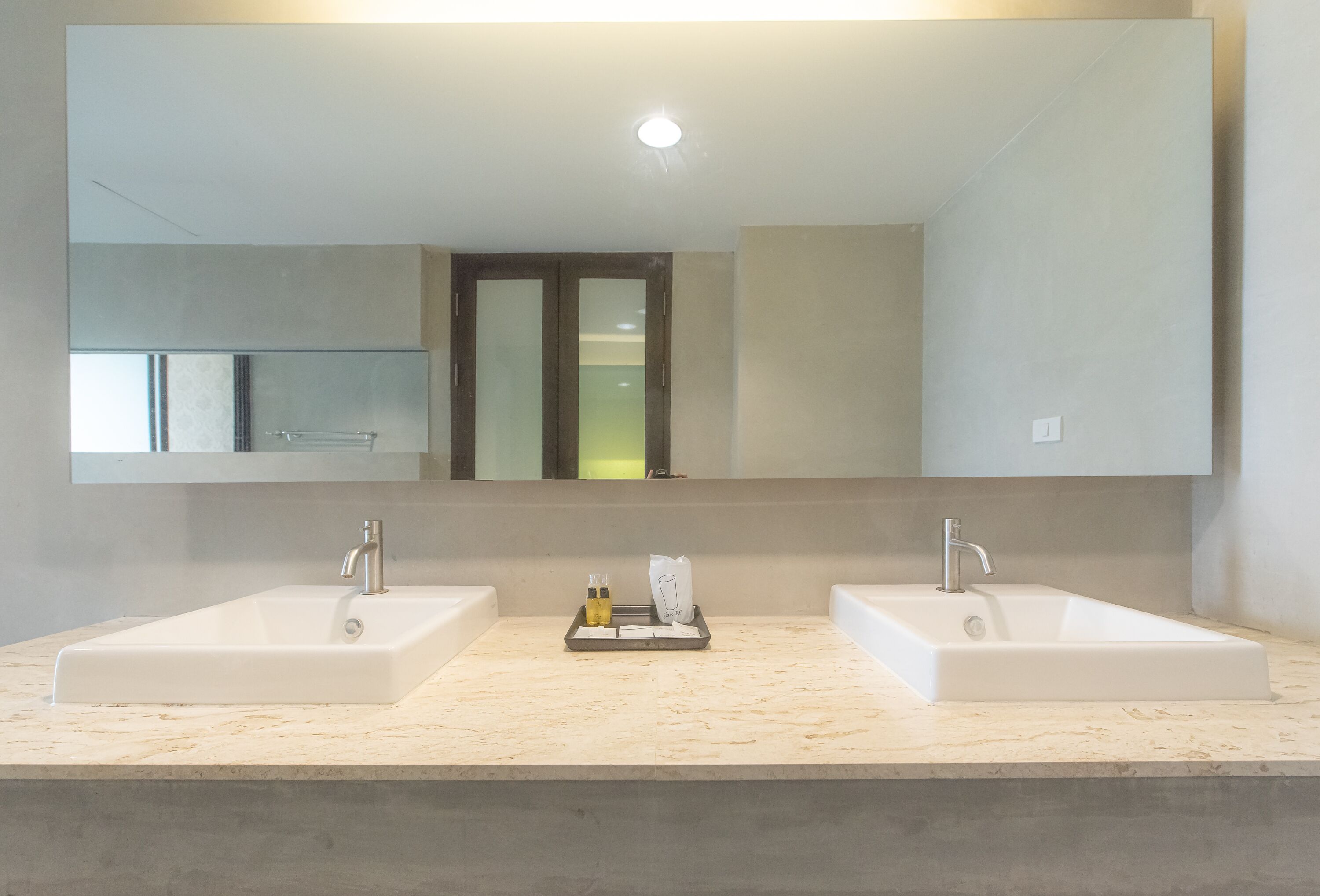 A modern bathroom with two sinks, a large mirror, and a tray with toiletries.