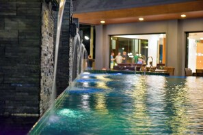 Une piscine intérieure agrémentée d’une cascade, entourée de murs en pierre et dotée d’un aménagement intérieur moderne.