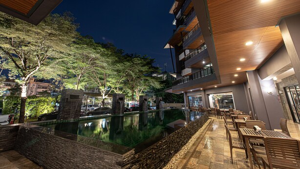 An outdoor pool area with a stone wall, wooden deck, and seating area. - The Proud Exclusive Hotel (Nakhon Pathom)
