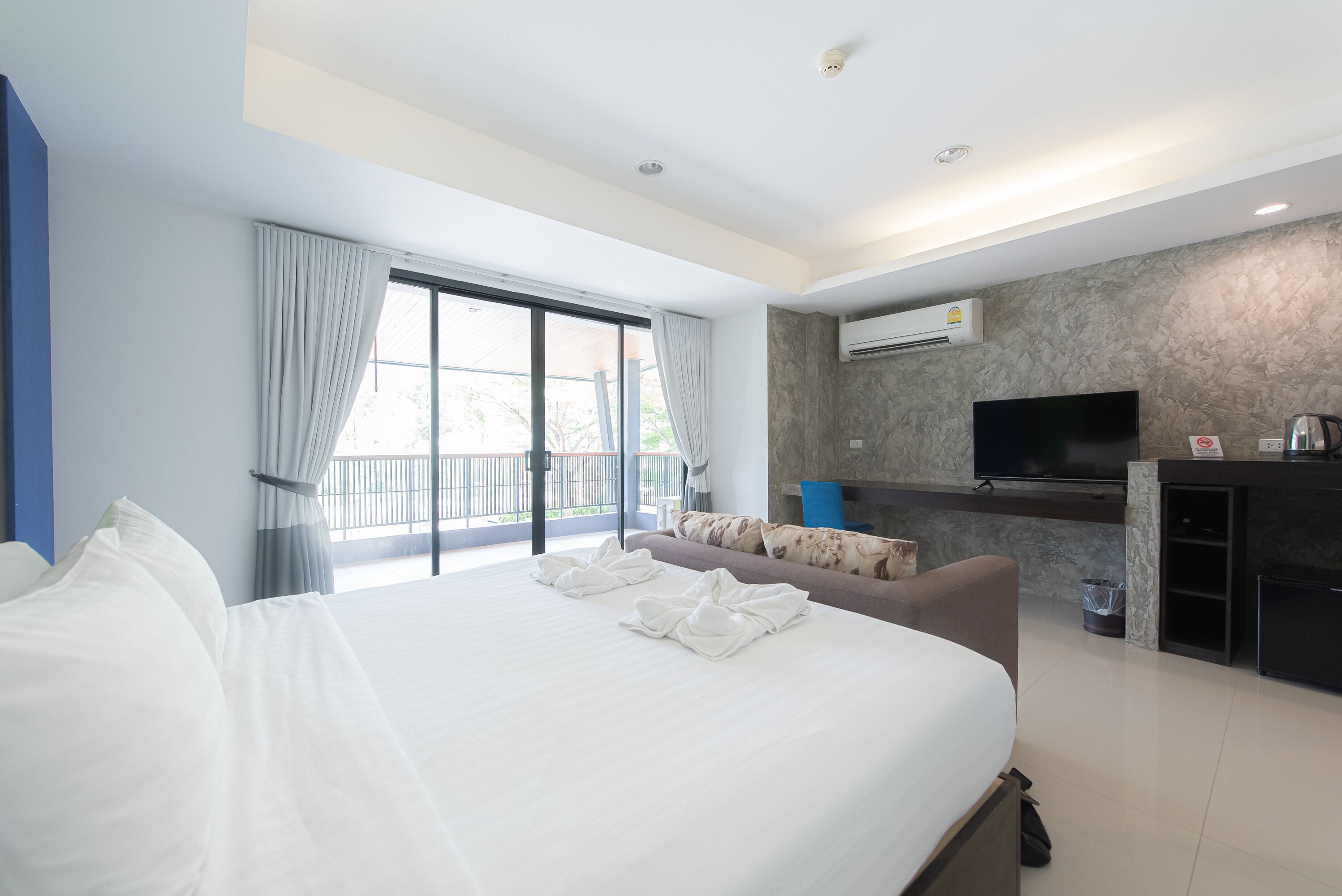 A hotel room with a large bed, a sofa, a TV, and a kitchenette.