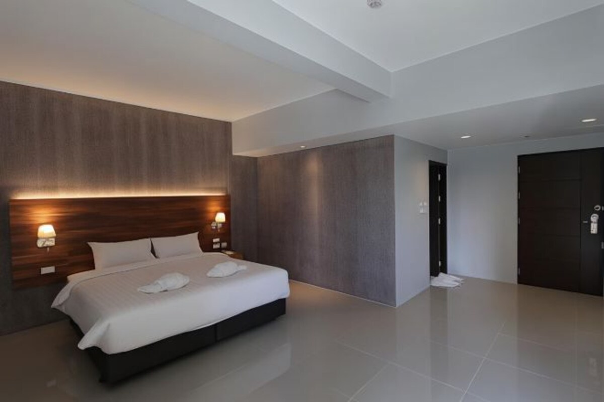 A modern hotel room with a large bed, built-in headboard, and wall-mounted lighting.