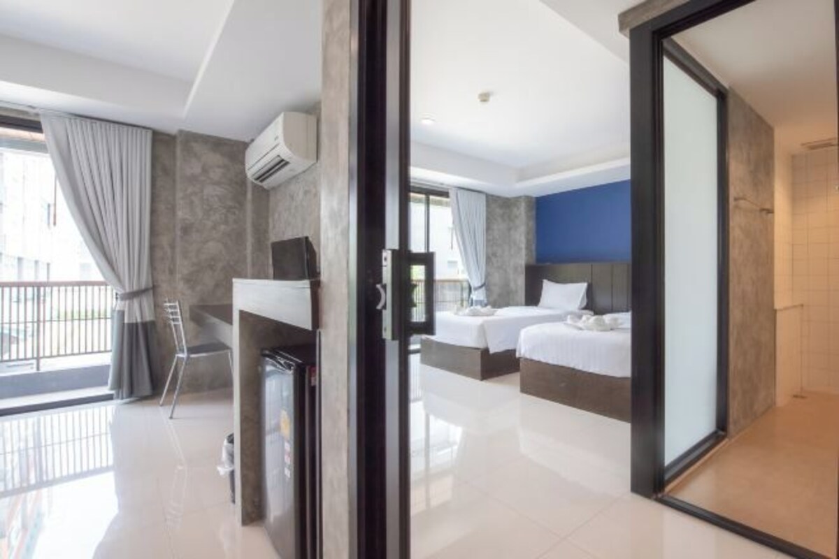 A modern hotel room with a balcony, a bed, a desk, and a large sliding glass door.