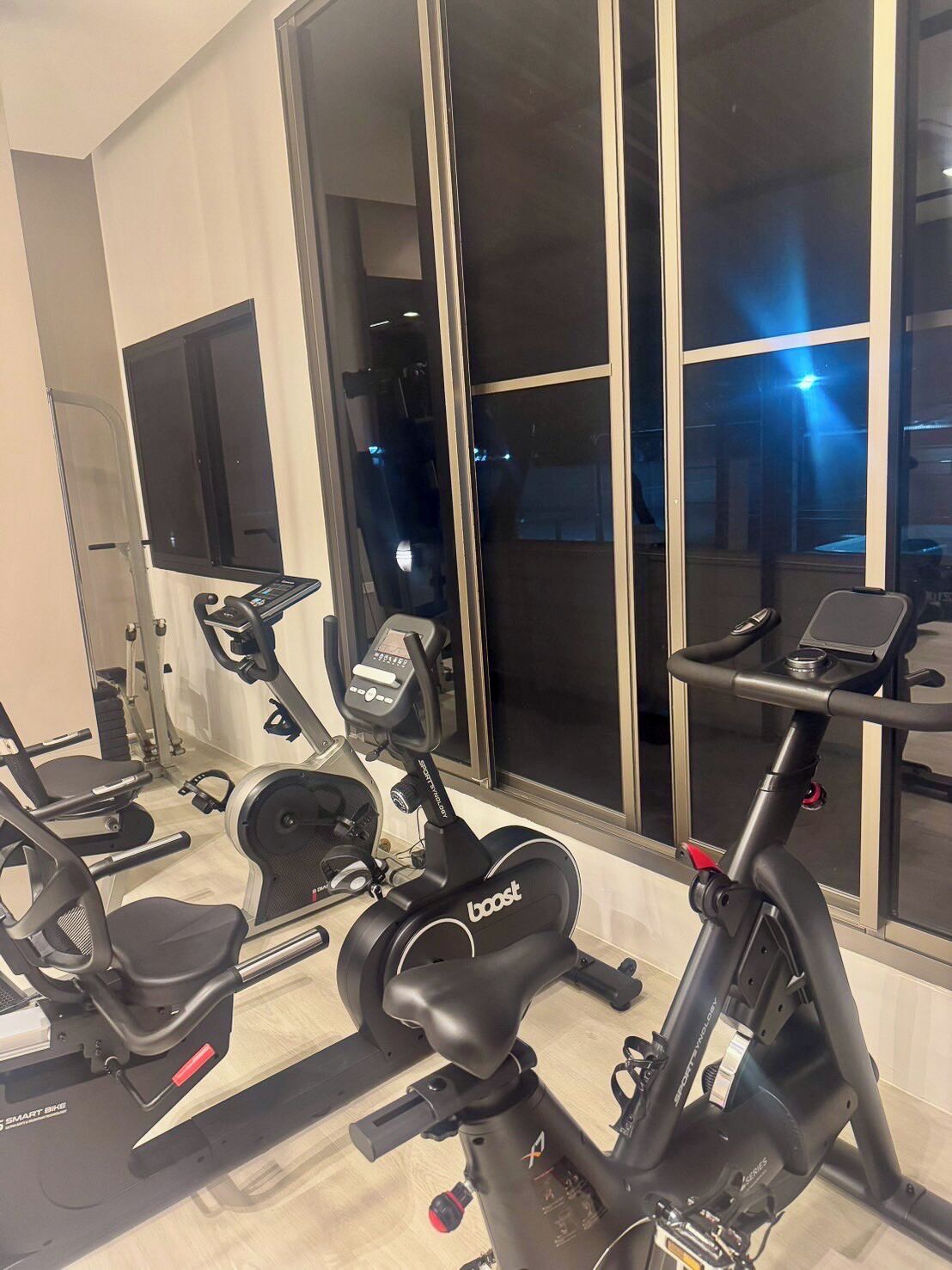 Een huisgym met diverse fitnessapparaten, waaronder een hometrainer, een elliptische trainer en een loopband.