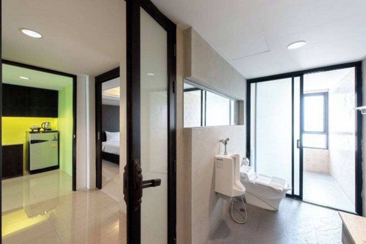 A modern hotel room with a large sliding glass door leading to a balcony, a built-in shower, and a small kitchenette area.
