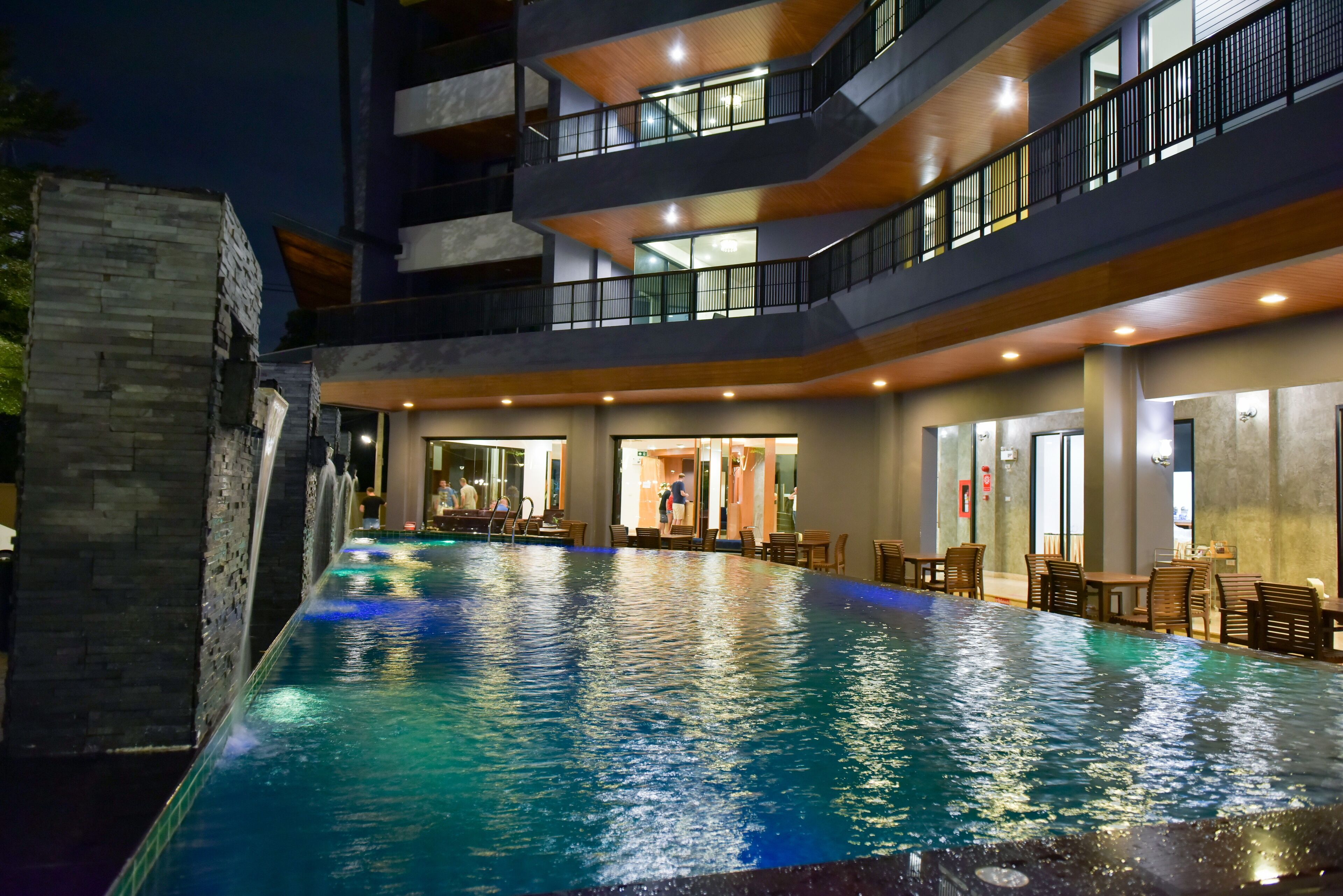 A modern hotel with a large indoor swimming pool, multiple floors, and outdoor seating areas.