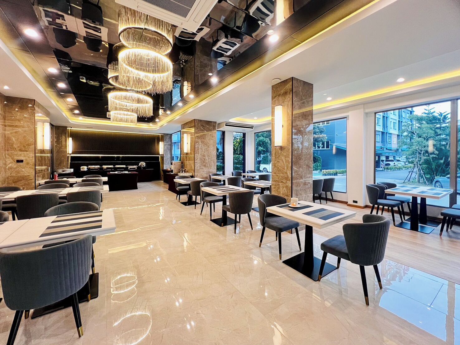 Um hall de hotel moderno com área de bar central, diversos arranjos de assentos e grandes janelas com vista para o exterior.