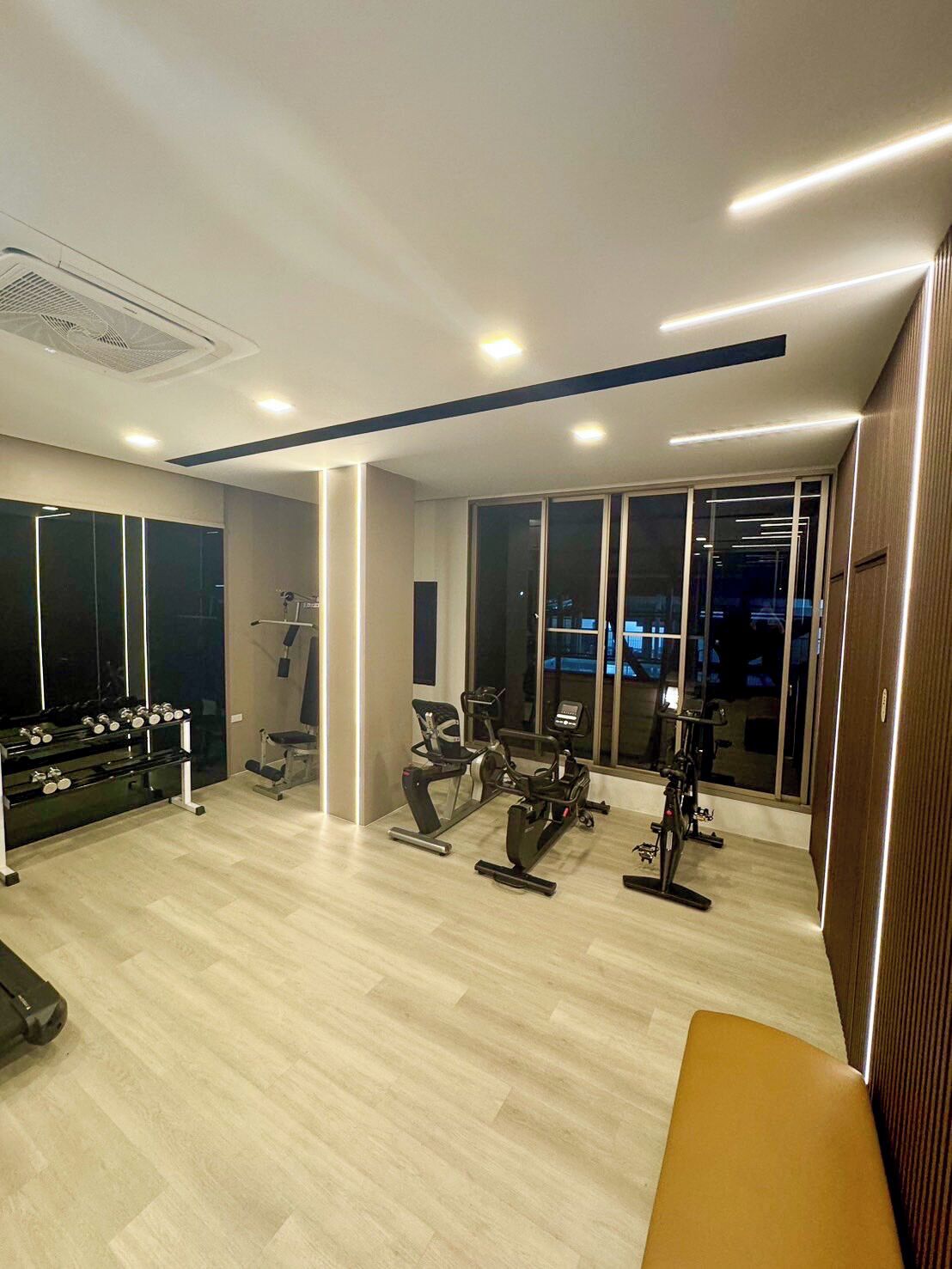 A modern gym with exercise equipment, large windows, and a bench.