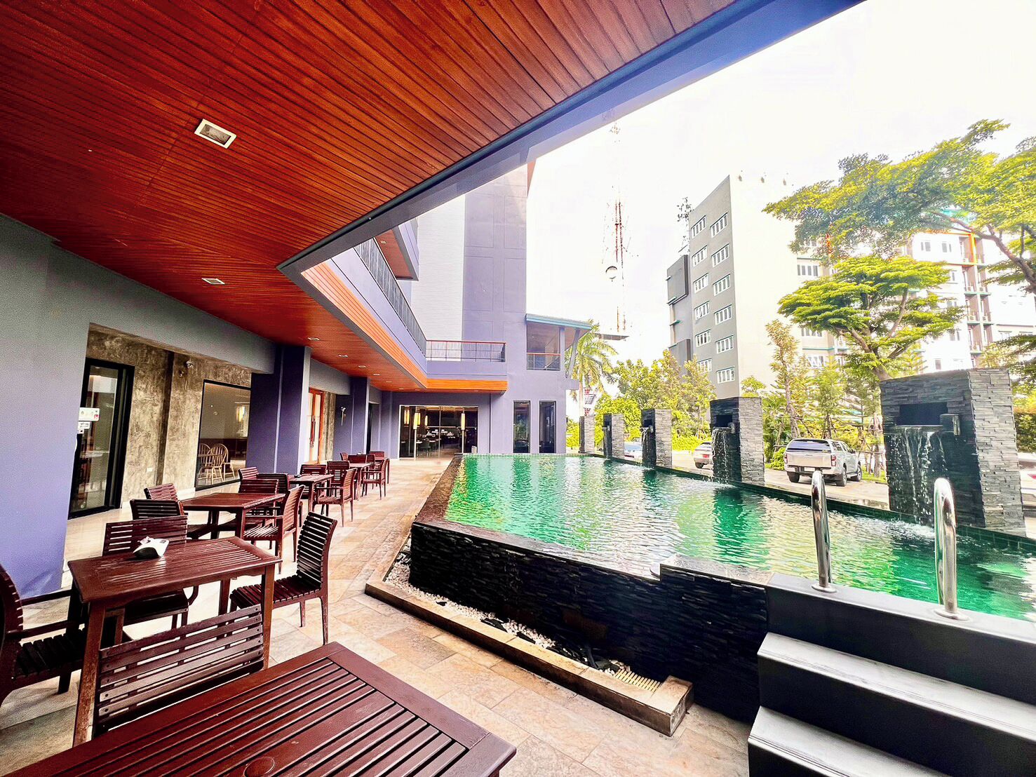 A modern outdoor pool area with a wooden deck, seating, and a view of surrounding buildings.