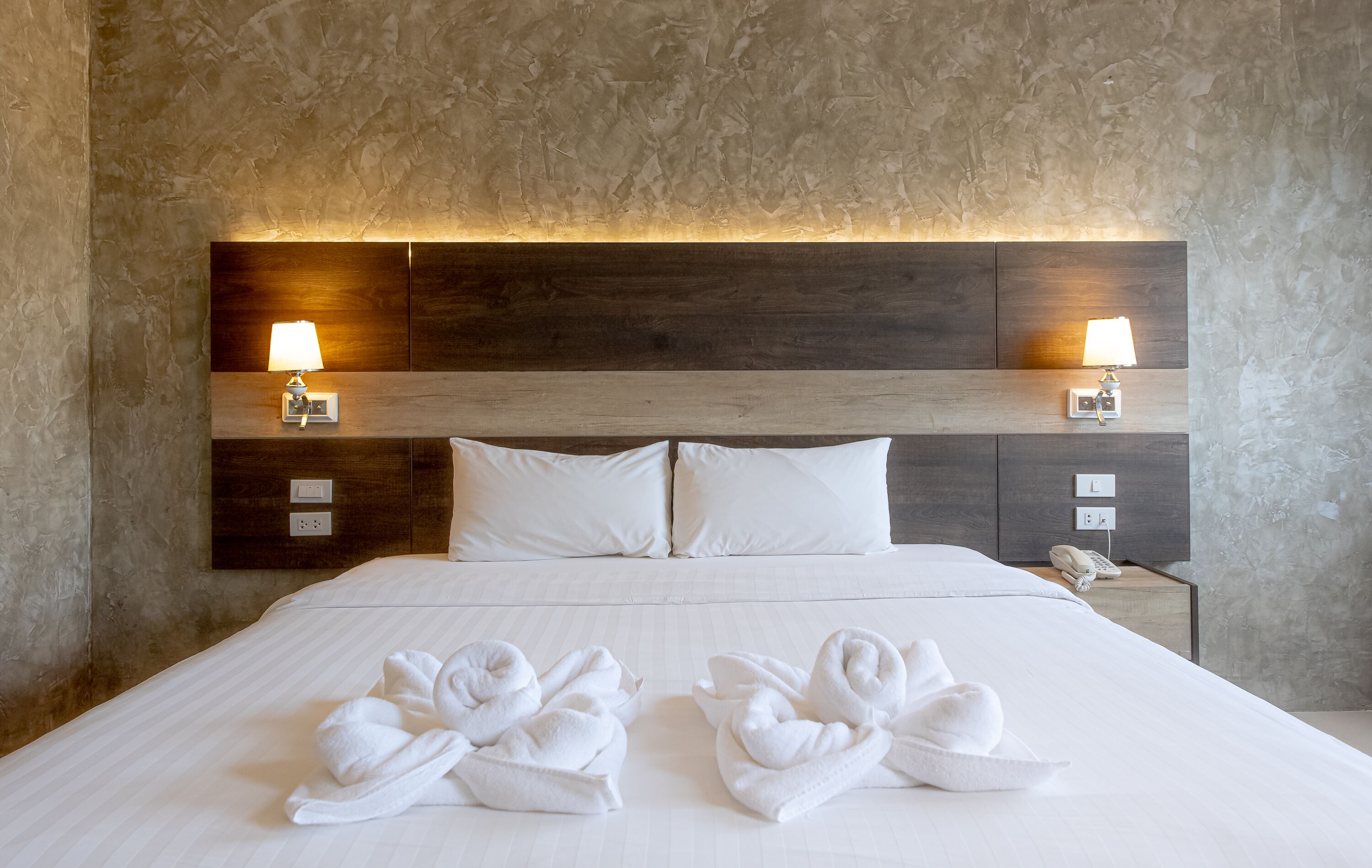 A hotel room with a large bed, two wall-mounted lamps, and two towels on the bed.