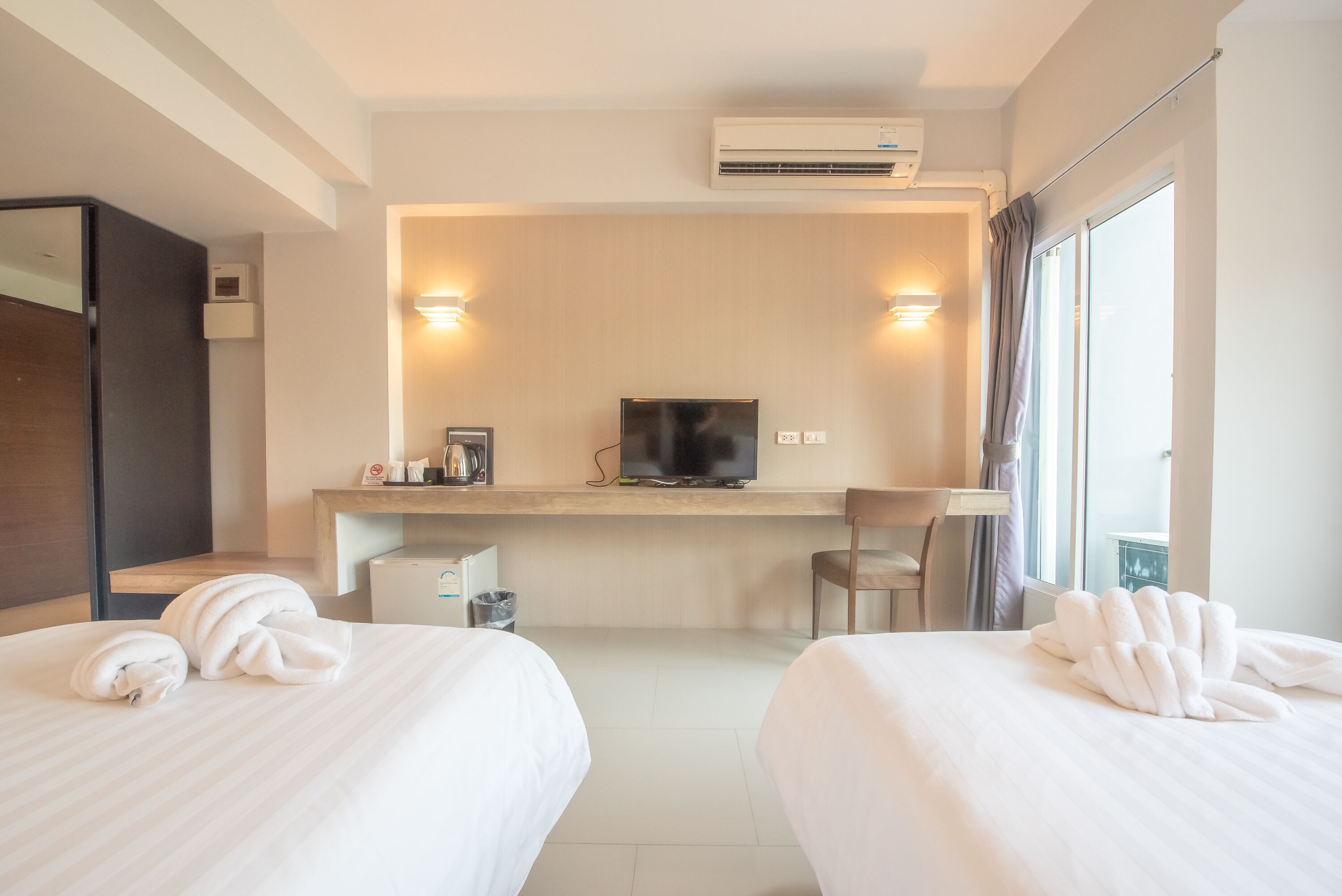 A hotel room with two beds, a desk with a TV, a chair, and a window with curtains.