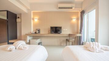 A hotel room with two beds, a desk with a TV, a chair, and a window with curtains.