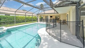 En swimmingpool med et overdækket område, omgivet af et hegn i metal, og med udsigt til en boligbygning i baggrunden.
