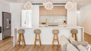 Une cuisine moderne dotée d’un îlot central, de tabourets de bar et d’un réfrigérateur en acier inoxydable.