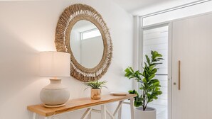 Une console en bois surmontée d’un vase blanc, d’une plante en pot et d’un miroir doté d’un cadre orné de franges.