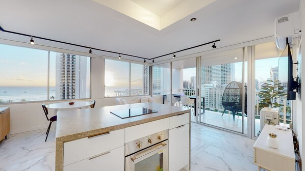 Une cuisine moderne dotée d’un grand îlot central, d’un coin repas et d’un balcon offrant une vue sur la ville.