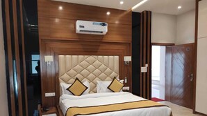 A hotel room with a large bed, a wooden headboard, an air conditioning unit, a bedside table, and a wardrobe. - Club 21by Sariska Fun city (Malakhera)