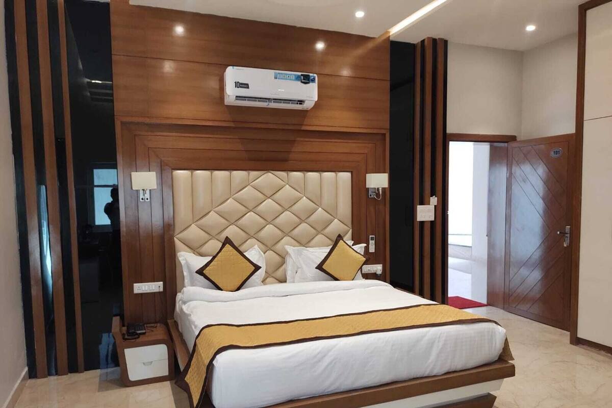 A hotel room with a large bed, a wooden headboard, an air conditioning unit, a bedside table, and a wardrobe.