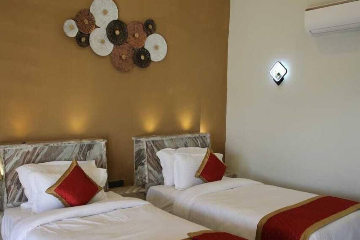 A hotel room with two beds, marble headboards, a decorative wall piece, and a patterned rug.
