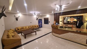 A hotel lobby with a reception desk, sofas, a coffee table, a ceiling fan, and a mounted deer head. - Club 21by Sariska Fun city (Malakhera)