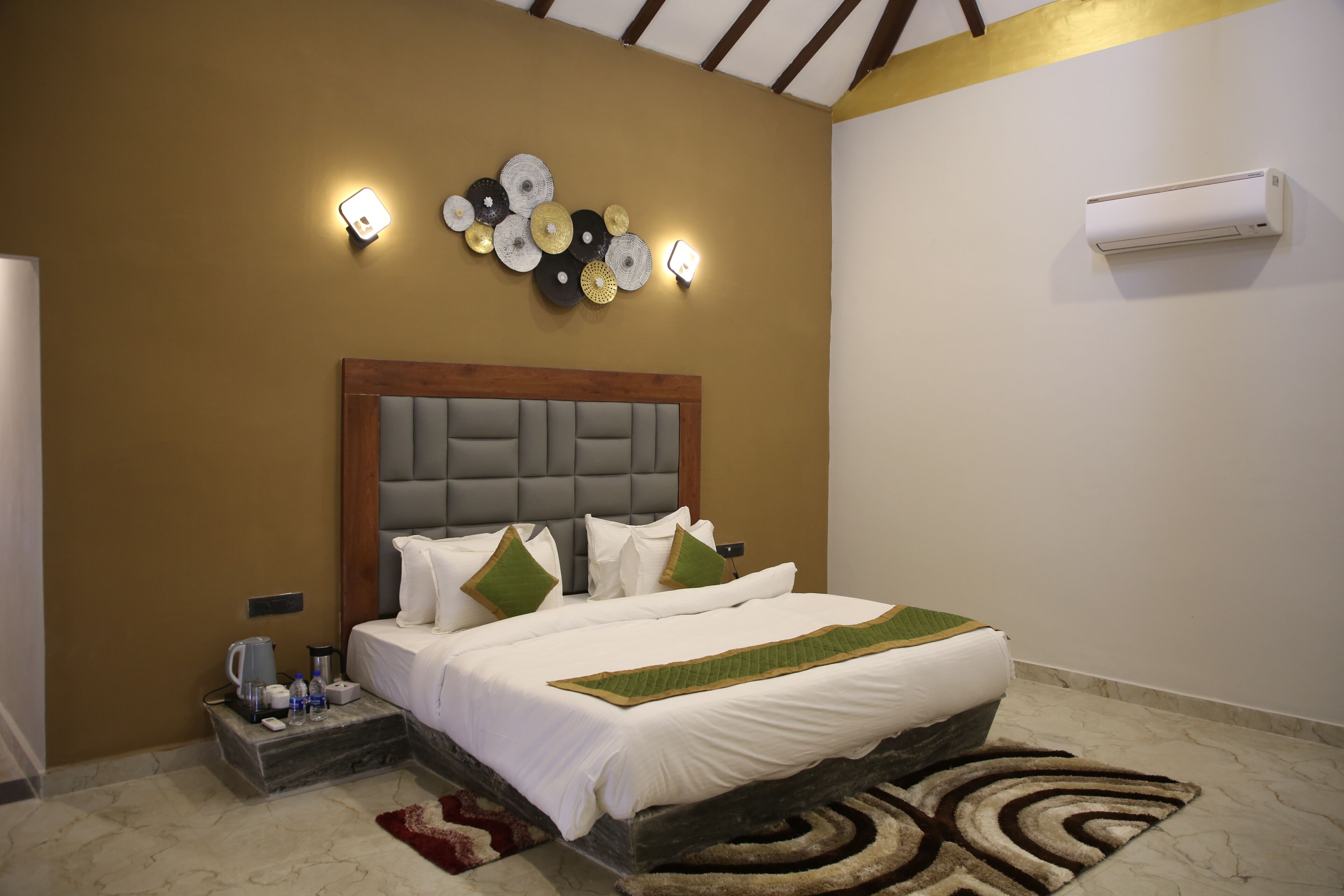Une chambre d’hôtel comprenant un lit, une table de chevet, un climatiseur fixé au mur, des éléments décoratifs sur les murs et un luminaire.