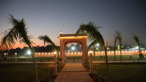 An outdoor pathway leading to a traditional archway with a lantern on top, surrounded by palm trees and well-lit by street lamps. - Club 21by Sariska Fun city (Malakhera)