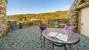A stone-walled patio with a round table and chairs, a book on the table, and a view of a green hillside. - Duddon View  -  Duddon Valley, Lake District (Dog-friendly) (Seathwaite)