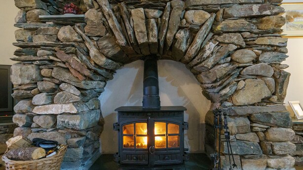 A stone fireplace with a wood-burning stove, a basket of firewood, and a fireplace tool on the right. - Duddon View  -  Duddon Valley, Lake District (Dog-friendly) (Seathwaite)