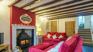 A cozy living room with a fireplace, red sofas, and a wooden staircase. - Riverside Cottage  - Duddon Valley (Dog-friendly) (Seathwaite)