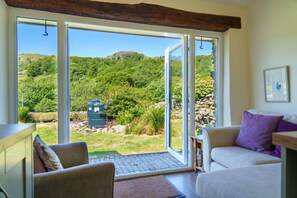 A room with a large sliding glass door leading to a garden with a water feature and a view of a hill.