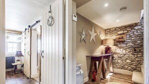 A hallway with a white door, a stone wall, and a lamp on a wooden table.