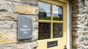 A stone building with a yellow door and a window. A sign on the wall reads "The Mustard Pot".
