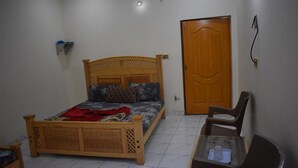 A bedroom with a wooden bed, a small table with chairs, a door, and a shelf with items. - Marwa Hotel and Restaurant (Abbottabad)